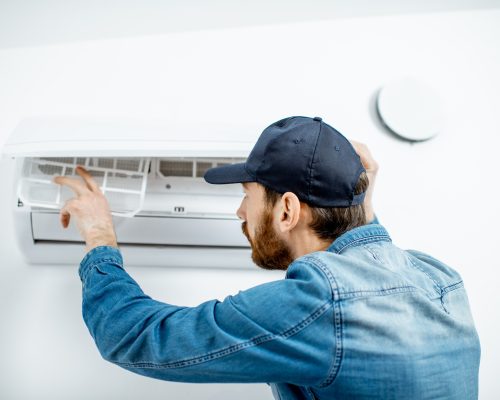 Repairman in blue workwear serving the air conditioner changing filter on the white wall background