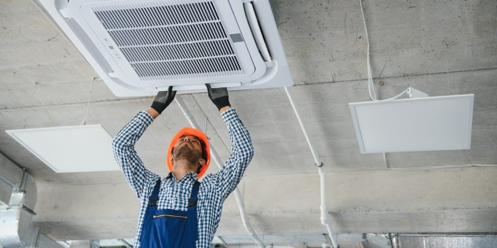 Concentrated young Indian engineer setting up air conditioner